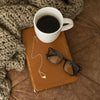 Valley gold necklace with brass pendant on Bible with glasses and mug of coffee