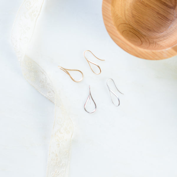 Storm Gold and silver teardrop shaped earrings next to wood bowl and lace ribbon